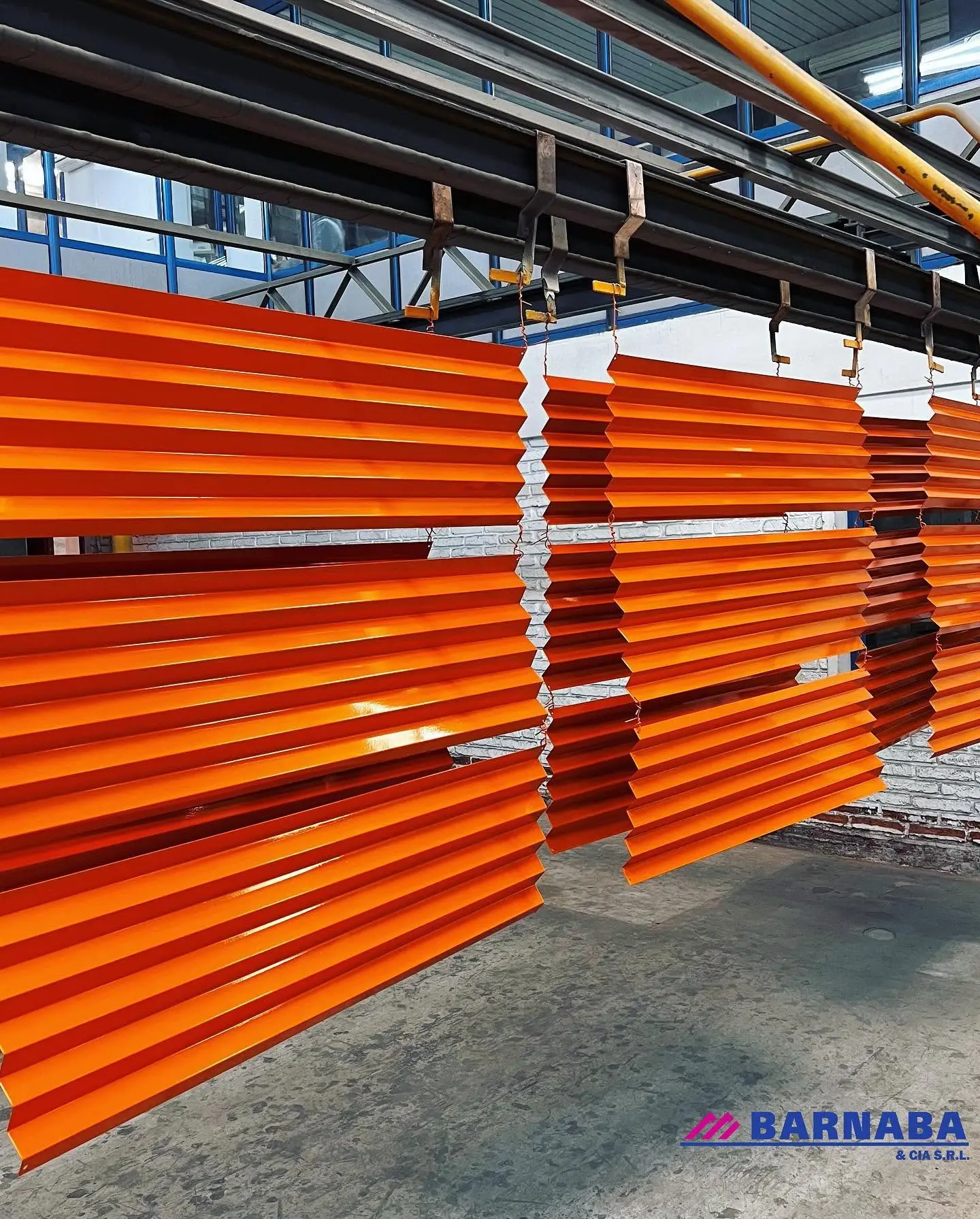 Perfiles de aluminio esmaltados en naranja colgados en la línea de producción